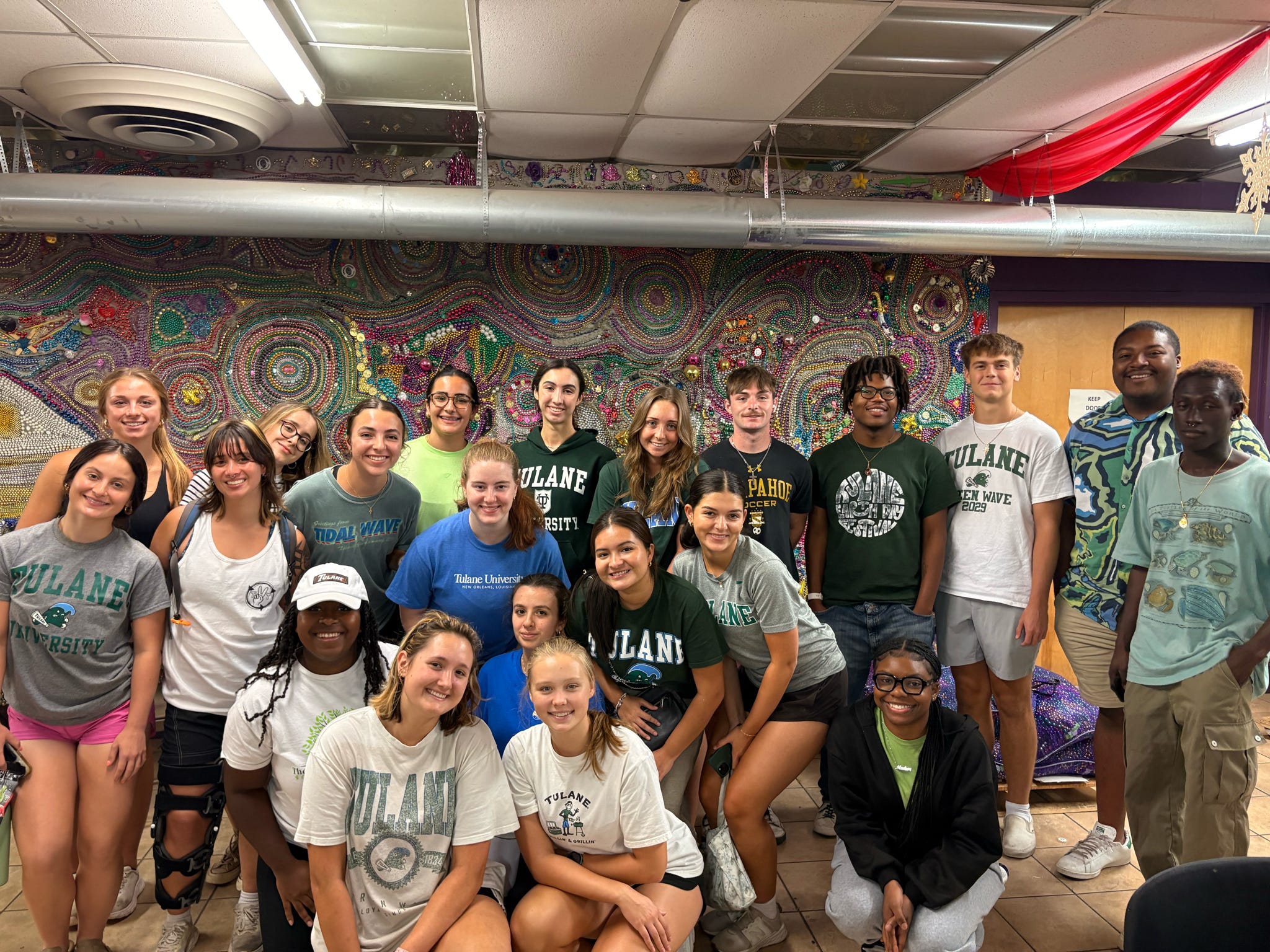 Smiling group of young adults wearing Dyland t-shirts in front of a colorful mosaic wall.